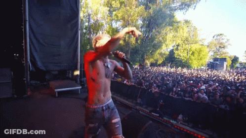 A Shirtless Man Is Singing Into A Microphone At A Concert GIF