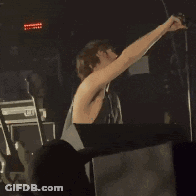 A Shirtless Man Is Singing Into A Microphone In Front Of A Crowd At A Concert GIF