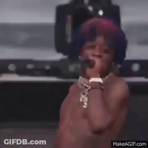 A Shirtless Man Is Singing Into A Microphone On A Stage . GIF