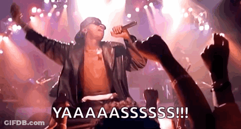 A Shirtless Man Is Singing Into A Microphone On A Stage While A Crowd Watches . GIF