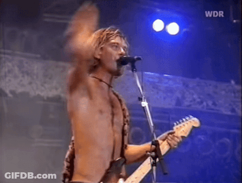 A Shirtless Man Is Singing Into A Microphone While Playing A Guitar GIF