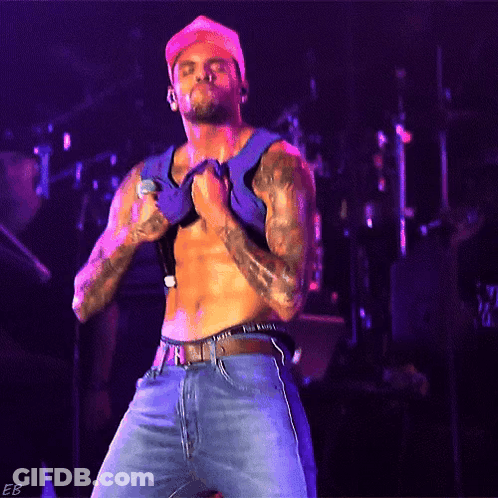 A Shirtless Man Is Singing Into A Microphone While Wearing A Hat GIF