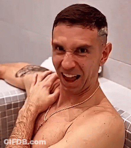 A Shirtless Man Is Sitting In A Bathtub Making A Funny Face While A Woman Holds His Arm . GIF