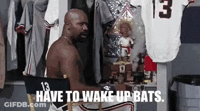 A Shirtless Man Is Sitting In A Chair With The Words Have To Wake Up Bats . GIF