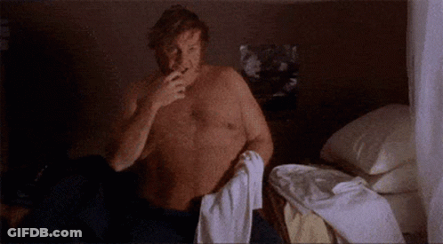 A Shirtless Man Is Sitting On A Bed With A Towel Around His Neck . GIF