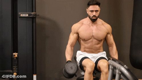 A Shirtless Man Is Sitting On A Bench Holding A Dumbbell With The Number 10 On It GIF