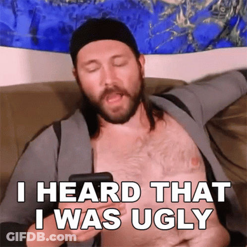 A Shirtless Man Is Sitting On A Couch Holding A Cell Phone And Says I Heard That I Was Ugly GIF