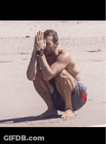 A Shirtless Man Is Squatting Down On The Beach GIF