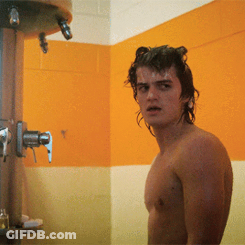A Shirtless Man Is Standing In A Bathroom Next To A Shower Head GIF