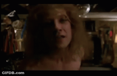 A Shirtless Man Is Standing In A Closet Holding A Bottle GIF