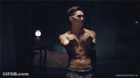 A Shirtless Man Is Standing In A Dark Room With His Arms Outstretched . GIF