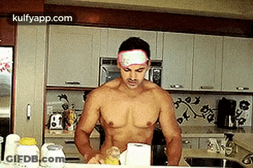 A Shirtless Man Is Standing In A Kitchen With A Bandage On His Forehead . GIF