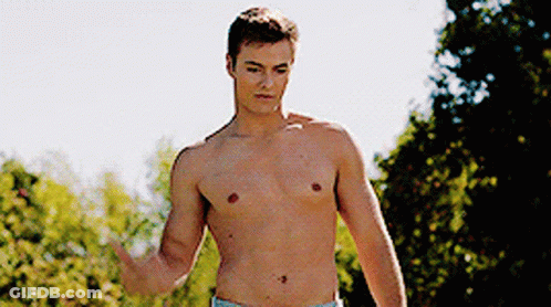 A Shirtless Man Is Standing In A Park With His Hand Outstretched GIF