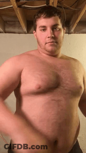 A Shirtless Man Is Standing In A Room With A Large Belly . GIF