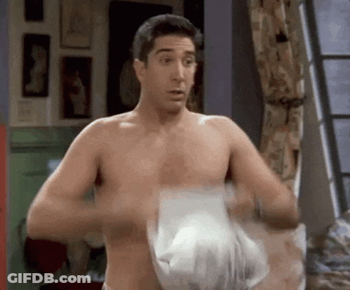 A Shirtless Man Is Standing In A Room With A Towel Around His Waist . GIF