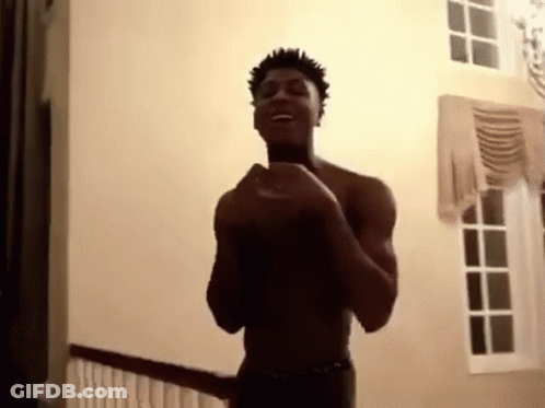A Shirtless Man Is Standing In A Room With His Hands In The Air . GIF