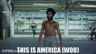 A Shirtless Man Is Standing In A Room With The Words `` This Is America ( Woo ) '' Written On The Screen . GIF
