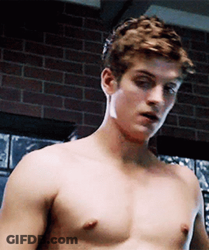 A Shirtless Man Is Standing In Front Of A Brick Wall In A Room . GIF