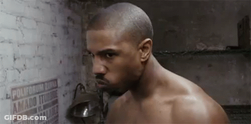A Shirtless Man Is Standing In Front Of A Brick Wall With A Lamp . GIF