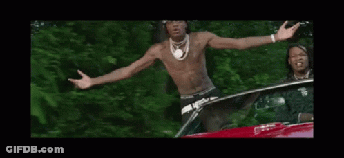 A Shirtless Man Is Standing In Front Of A Car With His Arms Outstretched And A Bandana On His Head . GIF