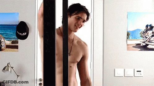 A Shirtless Man Is Standing In Front Of A Door With A Picture Of A Motorcycle On The Wall Behind Him . GIF