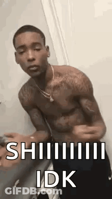A Shirtless Man Is Standing In Front Of A Door With His Arms Outstretched And A Necklace Around His Neck . GIF