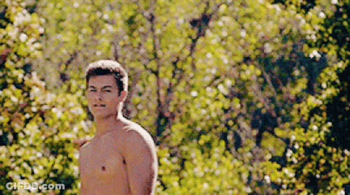 A Shirtless Man Is Standing In Front Of A Forest Of Trees GIF