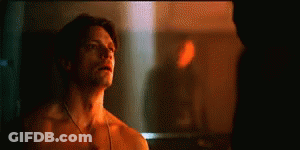 A Shirtless Man Is Standing In Front Of A Mirror And Looking At Himself . GIF