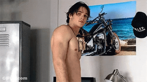 A Shirtless Man Is Standing In Front Of A Motorcycle Poster On A Wall . GIF