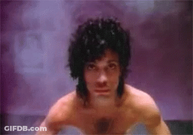 A Shirtless Man Is Standing In Front Of A Purple Wall . GIF