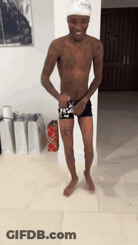 A Shirtless Man Is Standing In Front Of A Wall With A Picture On It GIF