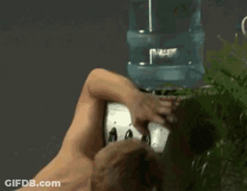 A Shirtless Man Is Standing In Front Of A Water Cooler . GIF