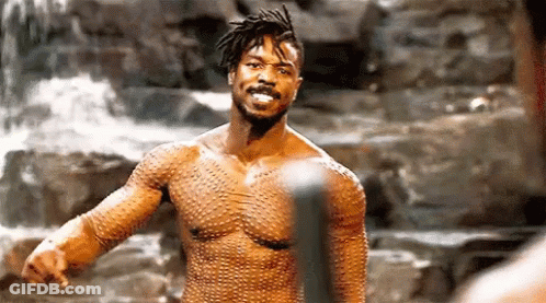 A Shirtless Man Is Standing In Front Of A Waterfall With His Arms Outstretched . GIF
