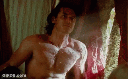 A Shirtless Man Is Standing In Front Of A Window And Looking At Himself . GIF