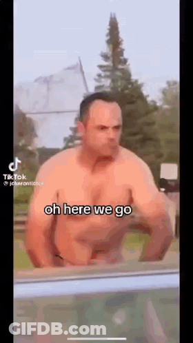 A Shirtless Man Is Standing In Front Of A Window With The Words `` Oh Here We Go '' Written On The Screen . GIF