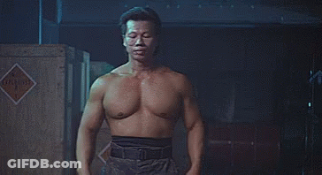 A Shirtless Man Is Standing In Front Of A Wooden Crate In A Dark Room . GIF