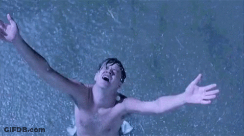 A Shirtless Man Is Standing In The Rain With His Arms Outstretched In The Air . GIF