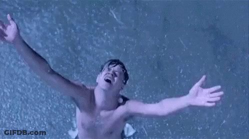 A Shirtless Man Is Standing In The Rain With His Arms Outstretched In The Air . GIF