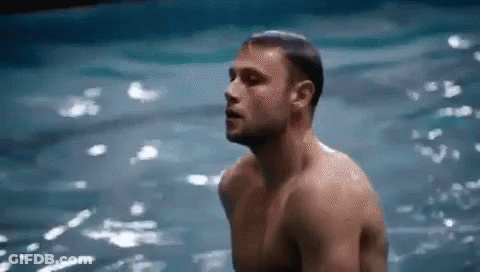 A Shirtless Man Is Standing In The Water With His Eyes Closed . GIF