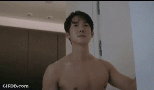 A Shirtless Man Is Standing Next To A Door In A Bathroom . GIF