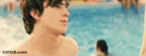 A Shirtless Man Is Standing Next To A Swimming Pool Looking At The Camera . GIF