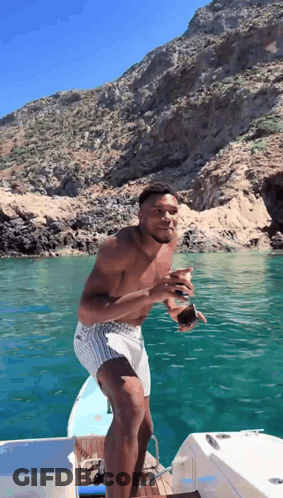 A Shirtless Man Is Standing On A Boat In The Ocean GIF