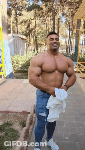 A Shirtless Man Is Standing On A Sidewalk Holding A Towel In His Hand . GIF