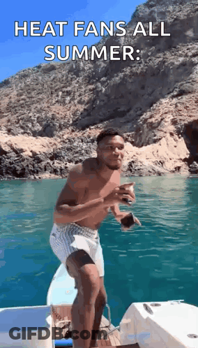 A Shirtless Man Is Standing On The Side Of A Boat In The Ocean . GIF