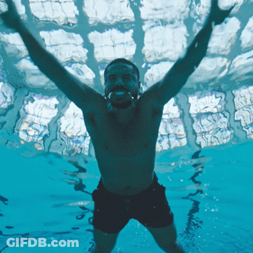 A Shirtless Man Is Swimming In A Pool With His Arms In The Air GIF