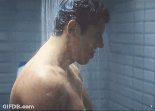 A Shirtless Man Is Taking A Shower In A Bathroom With A Shower Head . GIF