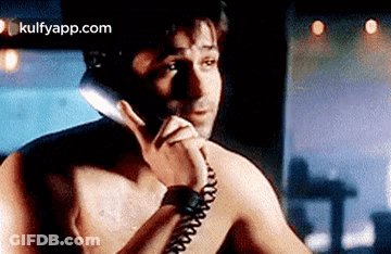 A Shirtless Man Is Talking On A Phone Without A Shirt On . GIF