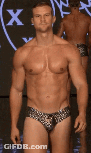 A Shirtless Man Is Walking Down A Runway In Front Of A Large X GIF