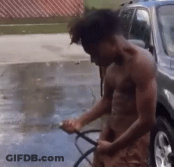 A Shirtless Man Is Washing A Car With A Hose In A Driveway . GIF
