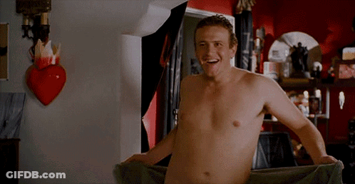 A Shirtless Man Is Wrapped In A Towel In A Bathroom And Smiling . GIF